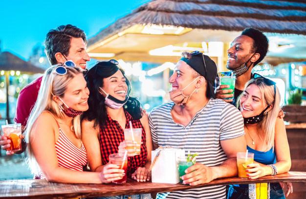 jovenes-amigos-internacionales-hablando-bar-cocteles-playa-mascarilla-abierta_101731-444